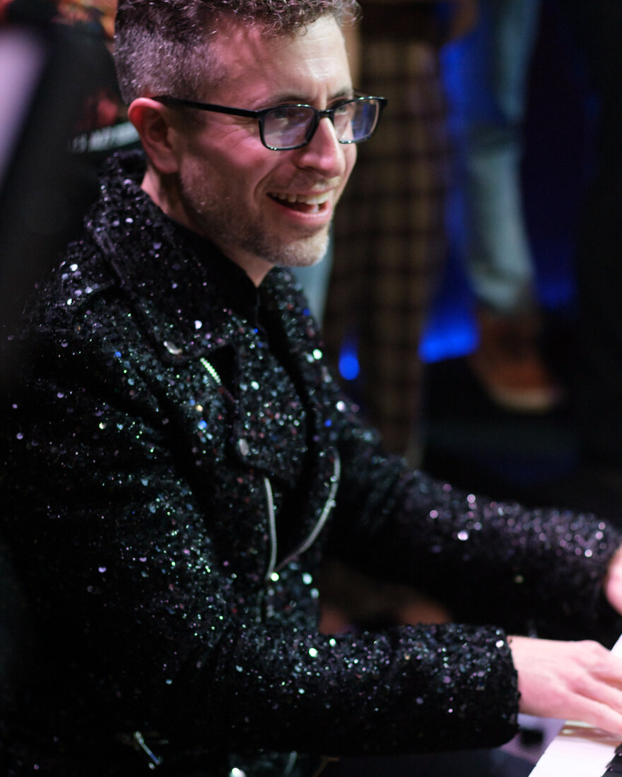 Greg Spero smiling at the keys, in a sequined jacket