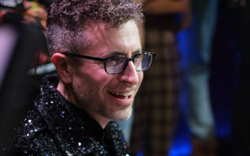 Greg Spero at the keys during the JammJam, smiling, in a sequined jacket