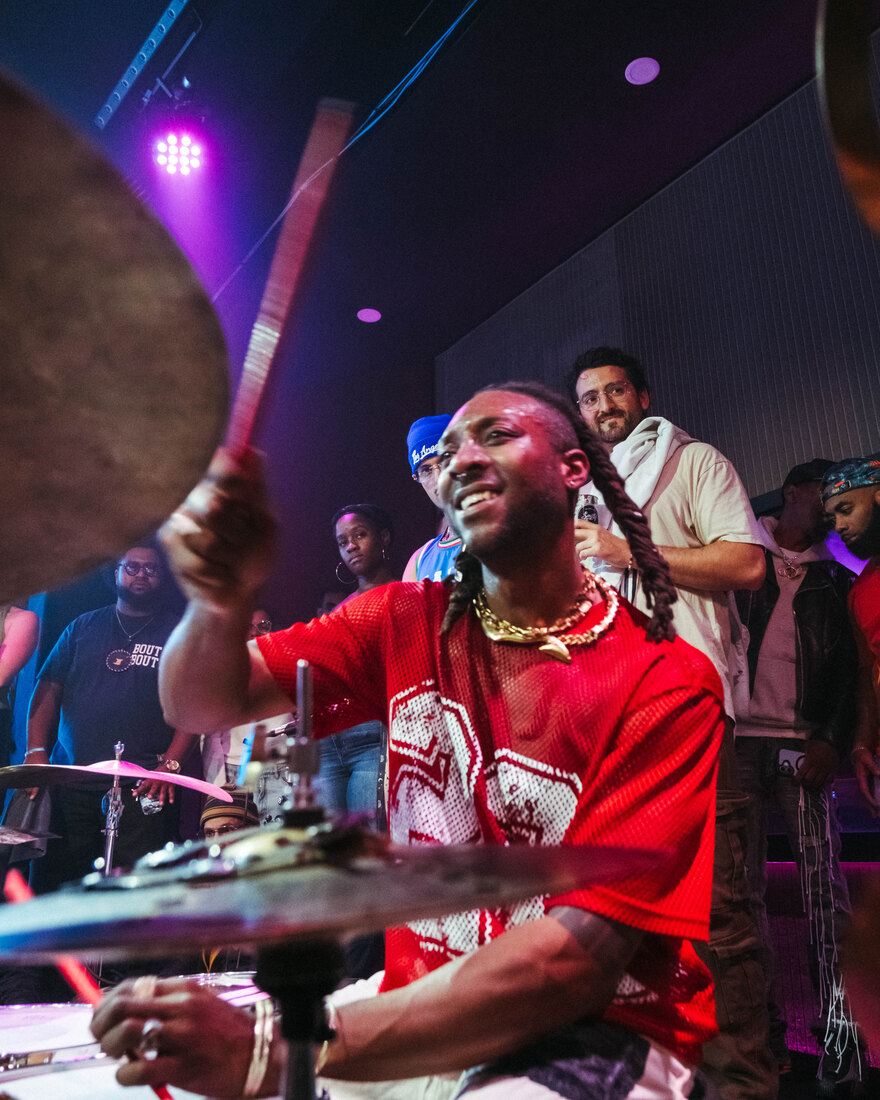 Mike Mitchell mid-strike at the drums, in a red jersey